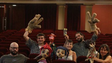 Imagen de títeres en un escenario, con estudiantes y docentes en el público