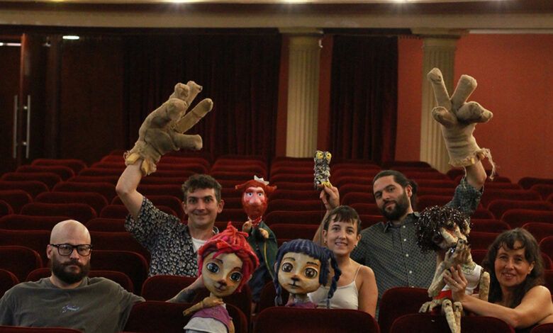 Imagen de títeres en un escenario, con estudiantes y docentes en el público